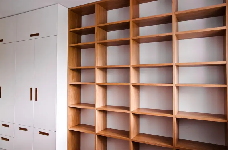 Raumhohe Regalwand aus Holz mit weißen Schrankfronten und Griffmulden