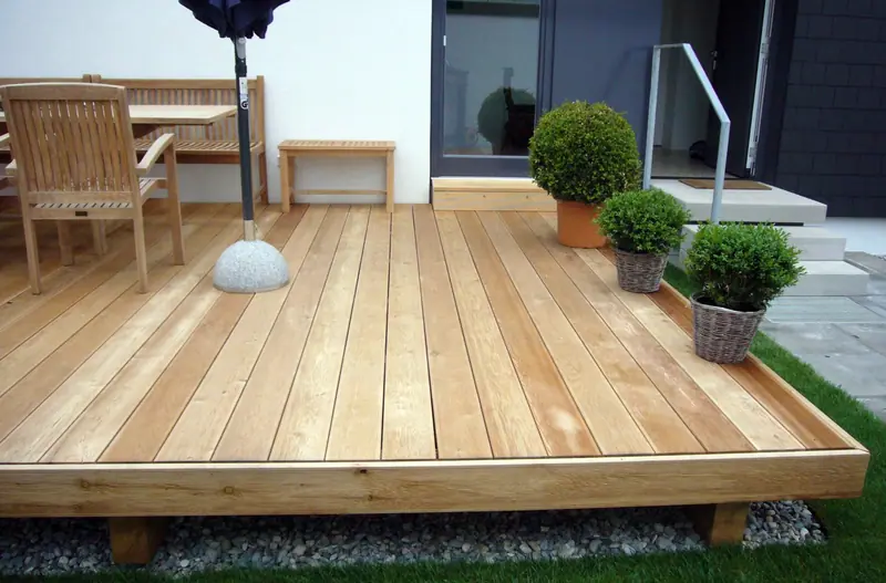Terrasse aus hellen Holzdielen neben Gartenmöbeln und Topfpflanzen