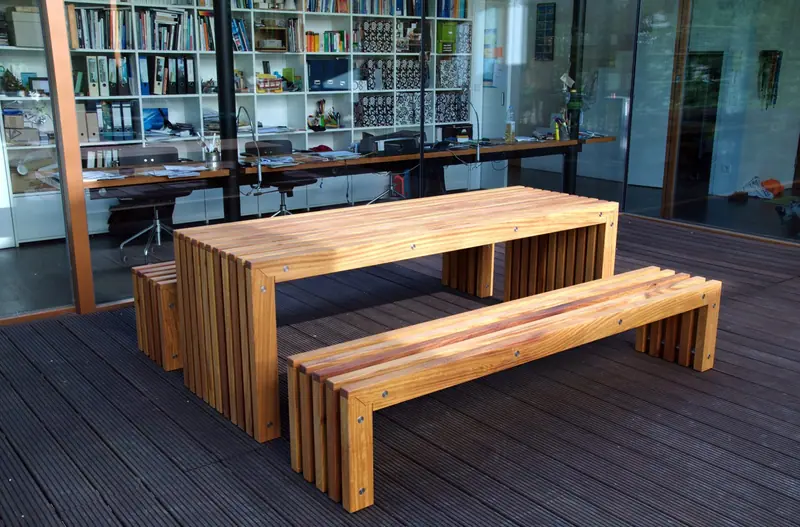 Langer Holztisch mit zwei Bänken auf einer Terrasse vor einer Glasfront